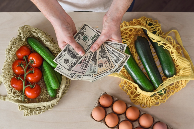 Hands holding us american money over produce and eggs.