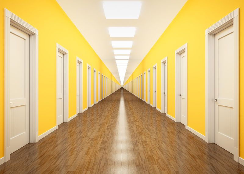 Image of a long corridor with bright yellow walls and white closed doors on each side running the length of the hall