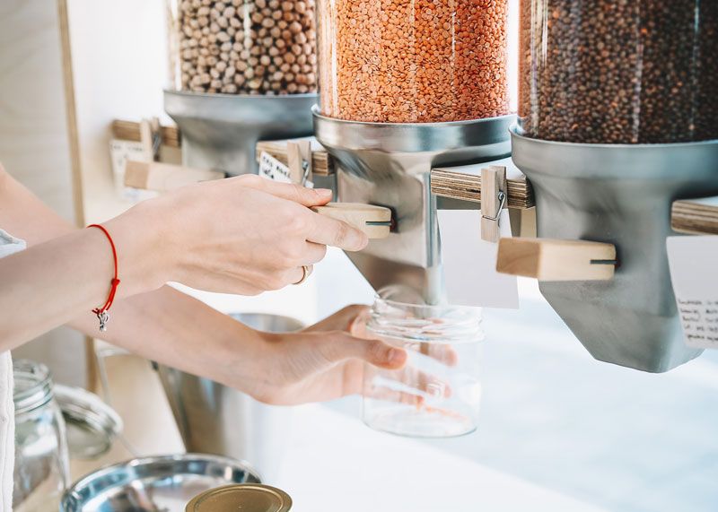 beans and grains displayed in glass dispensers in retail shop with customer dispensing product into glass container