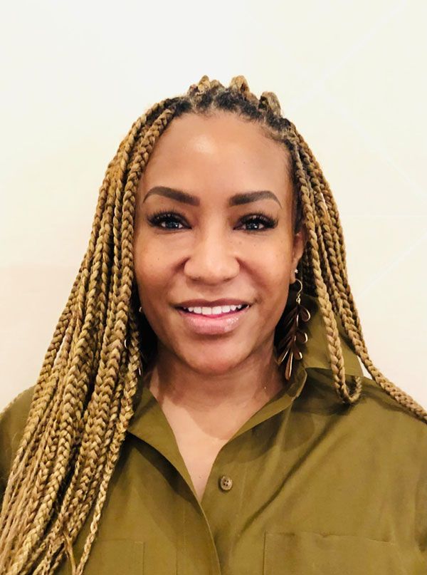 smiling woman with braids in her hair wearing an olive green shirt and hoop earrings